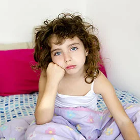 Girl sitting up in bed frowning because she has lice