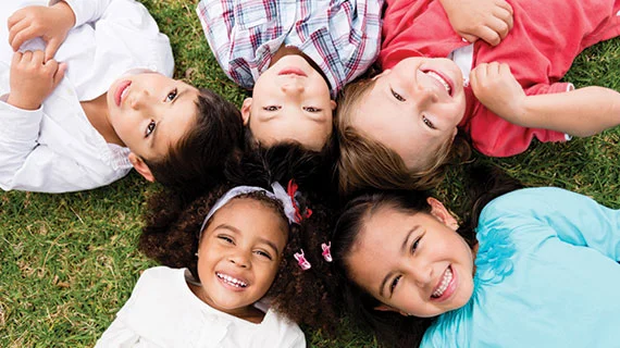 Children laying in the grass with their heads in a circle smiling together