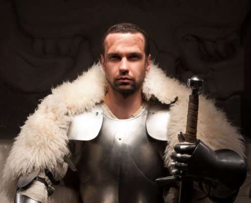 Man in medieval clothing with armor, fur, and a sword looking at the camera