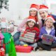 Family of four with Santa hats on opening presents by the Christmas tree