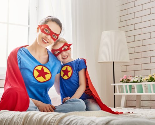 Mother and daughter dressed up as superheroes sitting in bed together