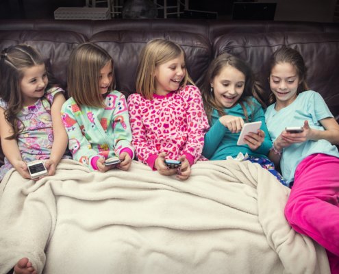 Five girls sitting on a couch smiling and looking at their phones