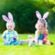 Two children wearing bunny ears sitting in the grass at an Easter egg hunt