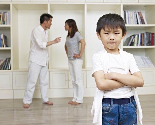 Parents arguing with each other in the background while a young child frowns