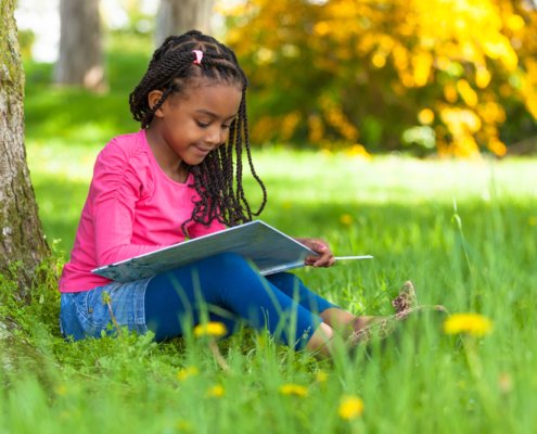 Girl sitting up against a tree reading a book