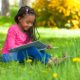 Girl sitting up against a tree reading a book