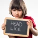 Young girl looking upset and holding a small chalk board that reads "head lice"