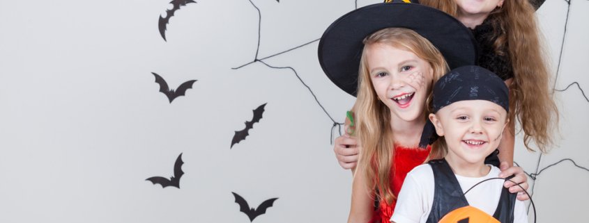 Three children dressed up as witches and a pirate for Halloween smiling together