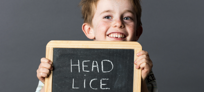 a boy smiling holding a chalkboard explaining that he has head lice