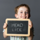 a boy smiling holding a chalkboard explaining that he has head lice